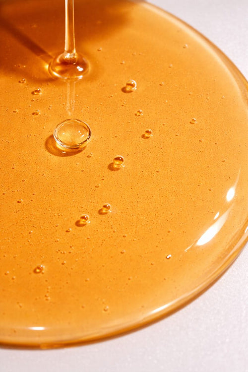 Close-up of golden oil texture with droplets on a white background